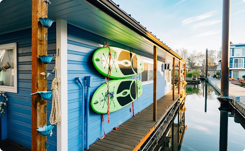 A Beautiful blue home with green Paddle boards secured to its side at island Cove Marina in Portland Oregon